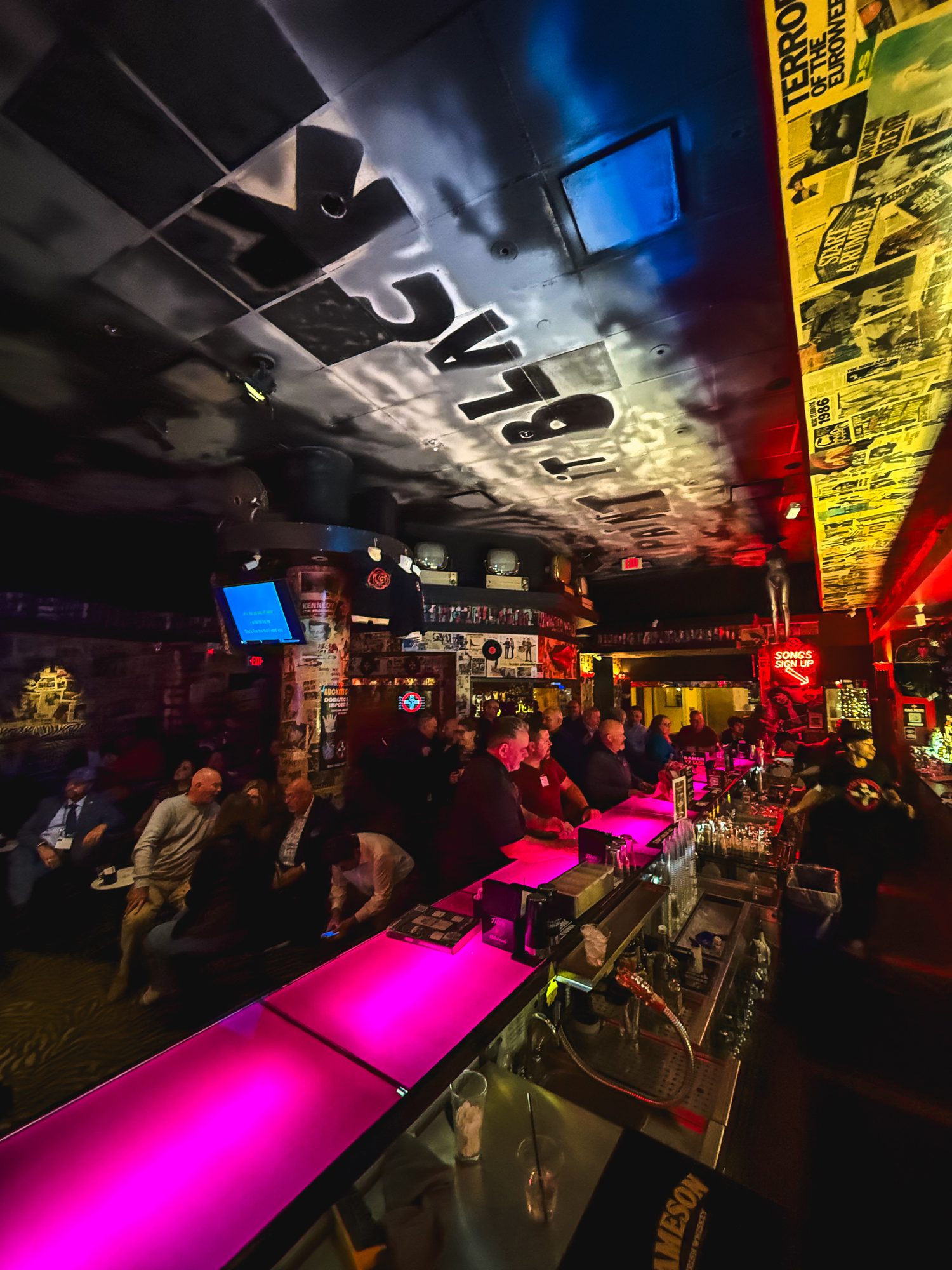 The long neon-pink bar at Planet Rose, packed with guests under the black-lettered ceiling